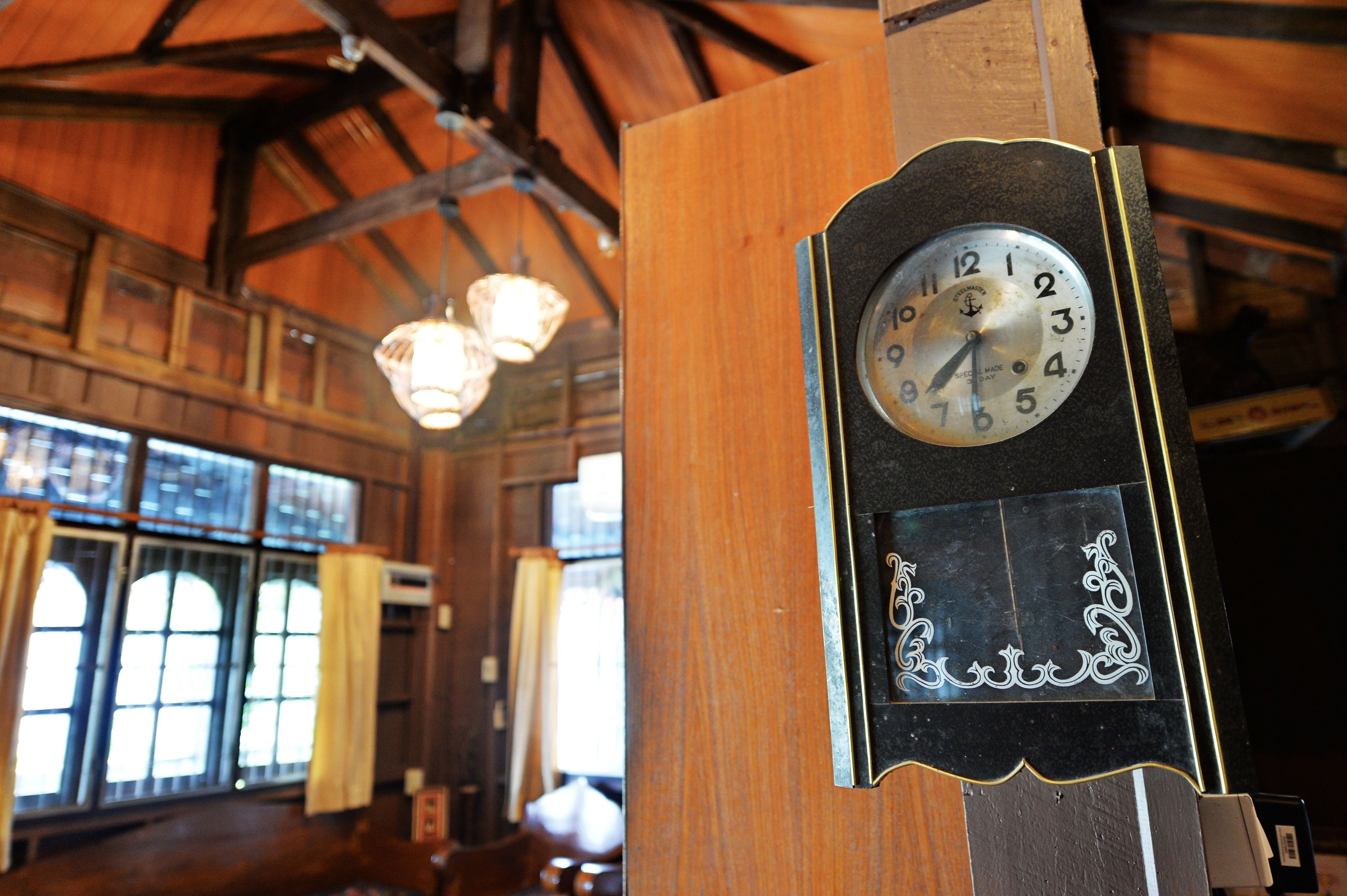 A clock mounted on a wooden post inside a building with large windows and wooden beams.