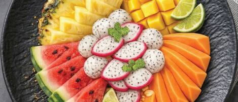 A fruit platter with pineapple, mango, watermelon, dragon fruit, and lime on a dark plate.