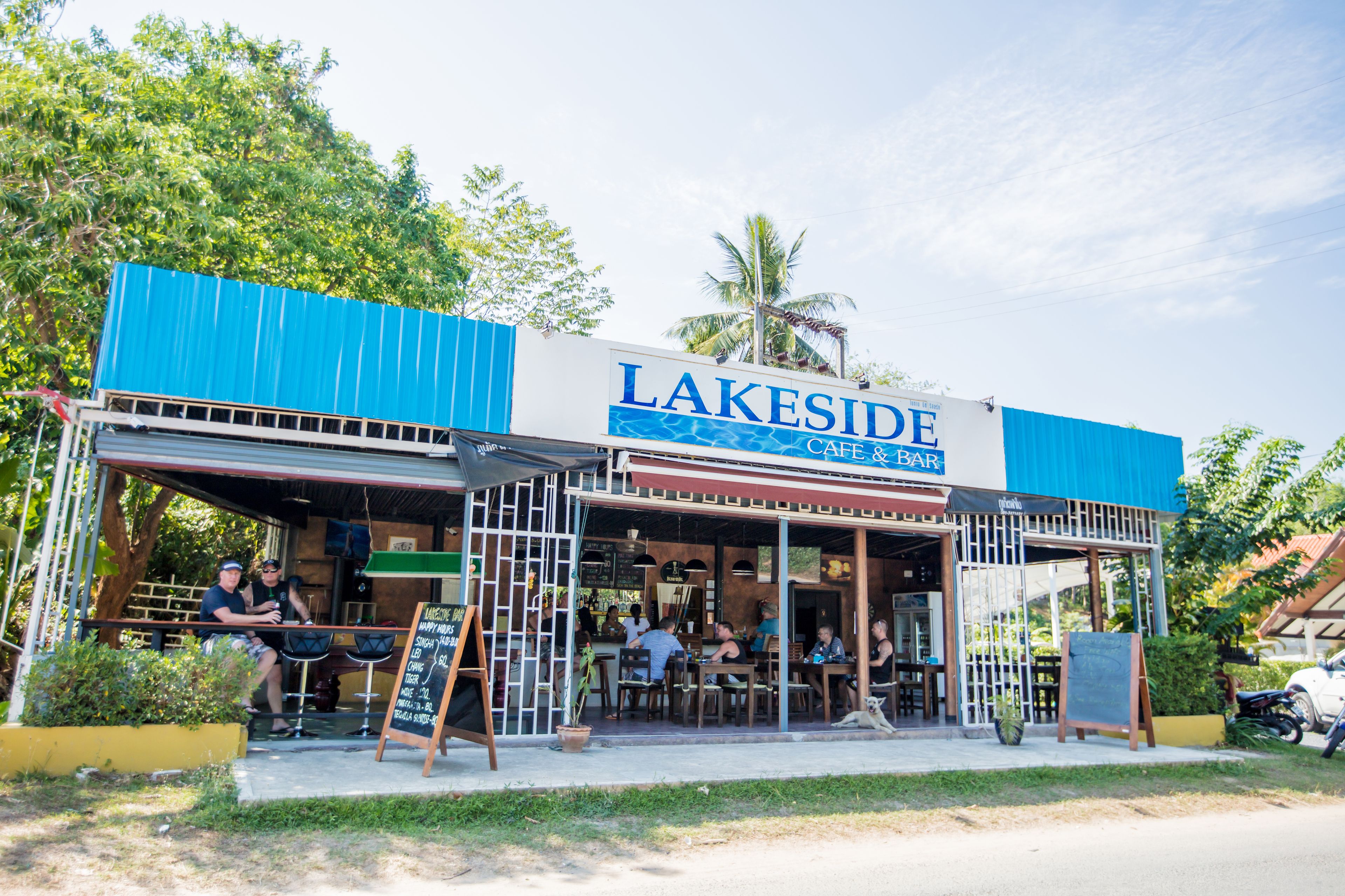 A lakeside cafe & bar with outdoor seating and a blue awning.