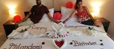 A bed with personalized decorations including the names "Milandeep" and "Birinder" and the words "Happy Honeymoon" and "Birthday".