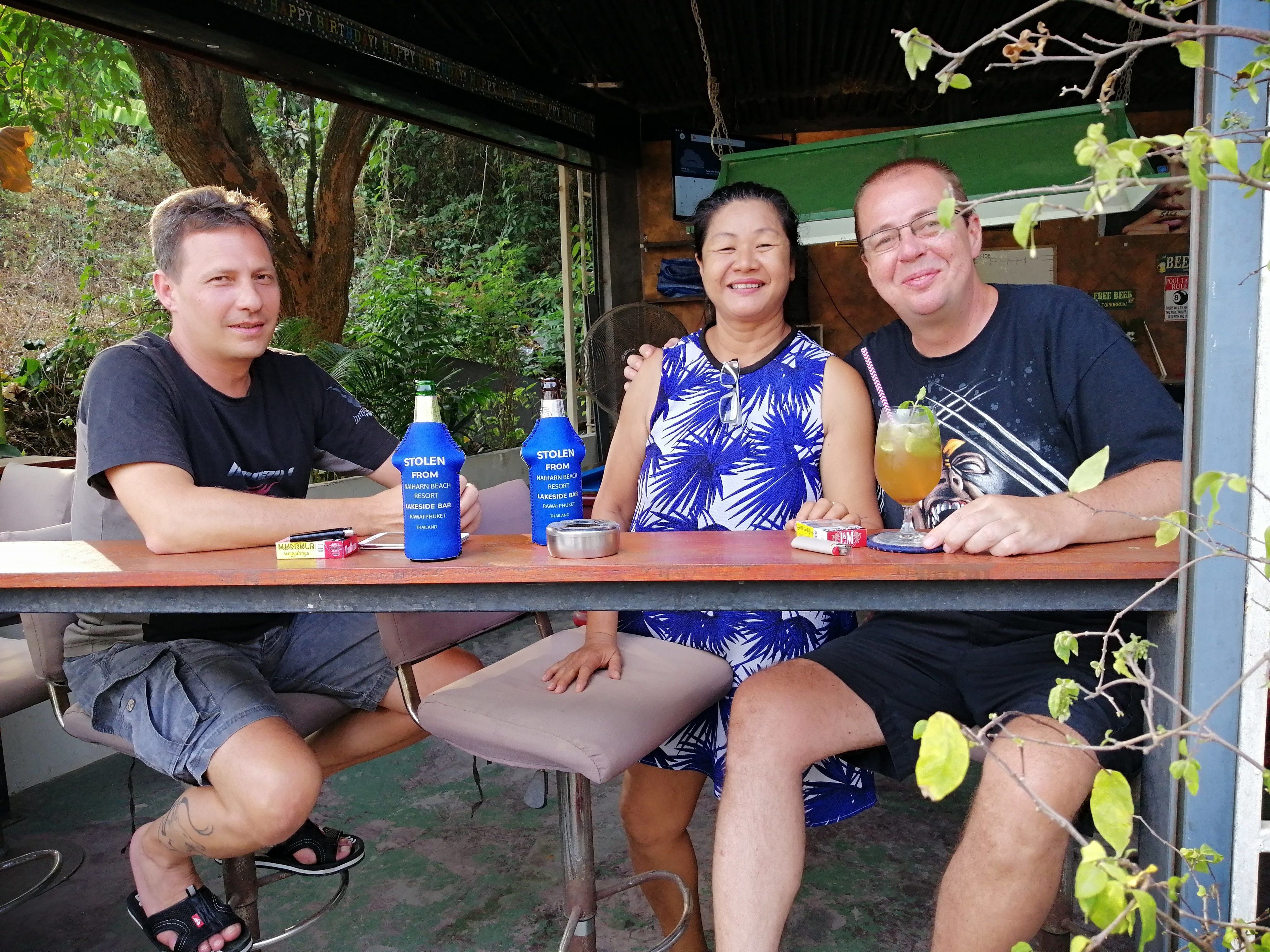 Three people seated at an outdoor table with drinks and a menu.