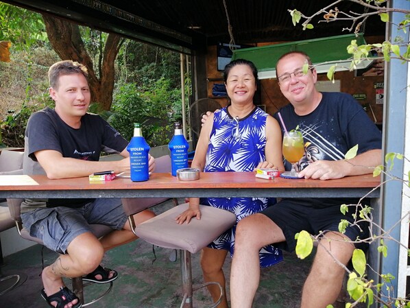 Tres personas sentadas en una mesa al aire libre, con bebidas y una carta.