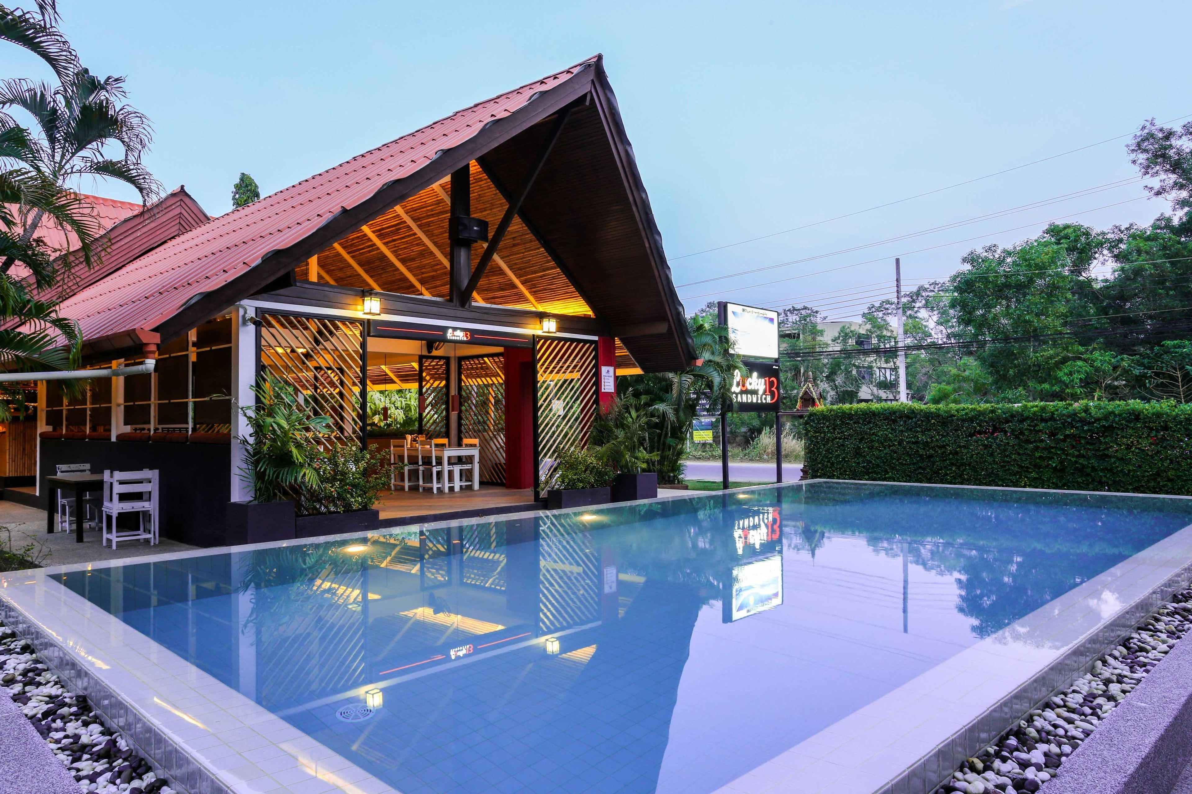 A modern building with a red roof and glass walls, adjacent to a clear swimming pool.
