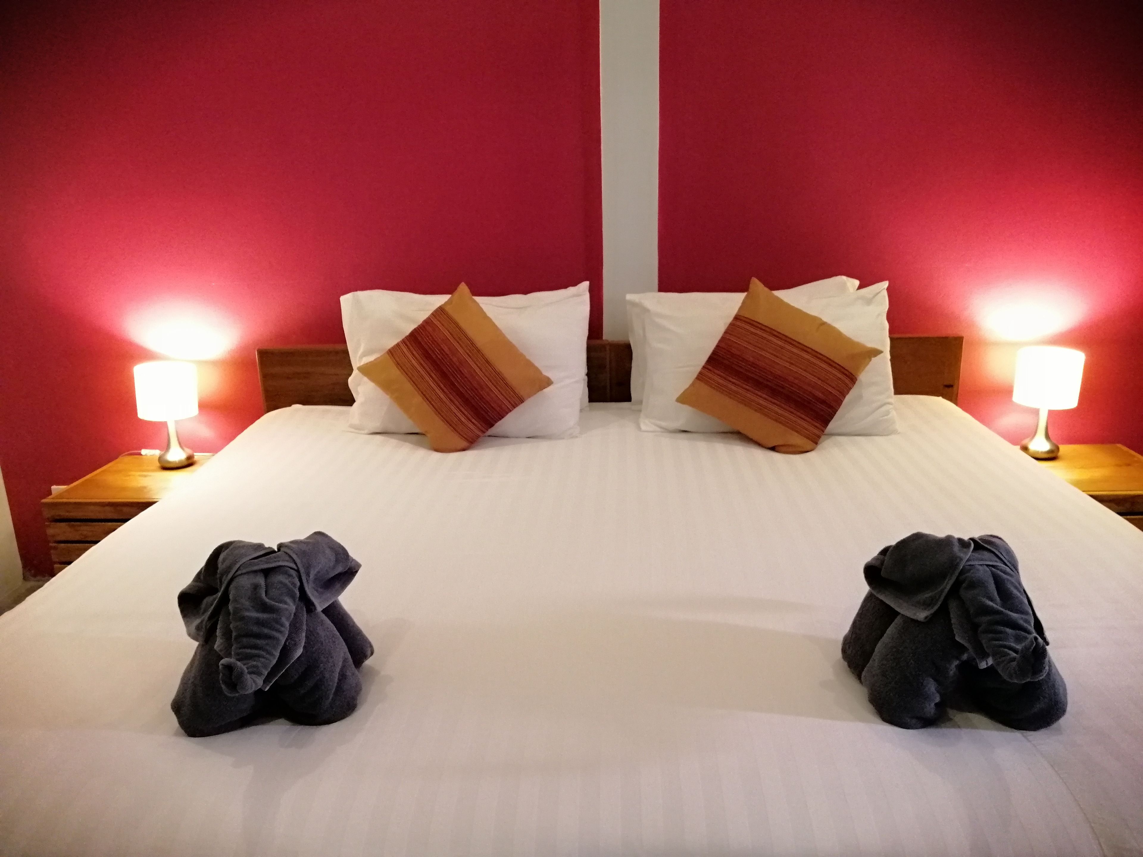 A hotel room with a large bed, two pillows, two bedside lamps, and two folded towels on the bed.