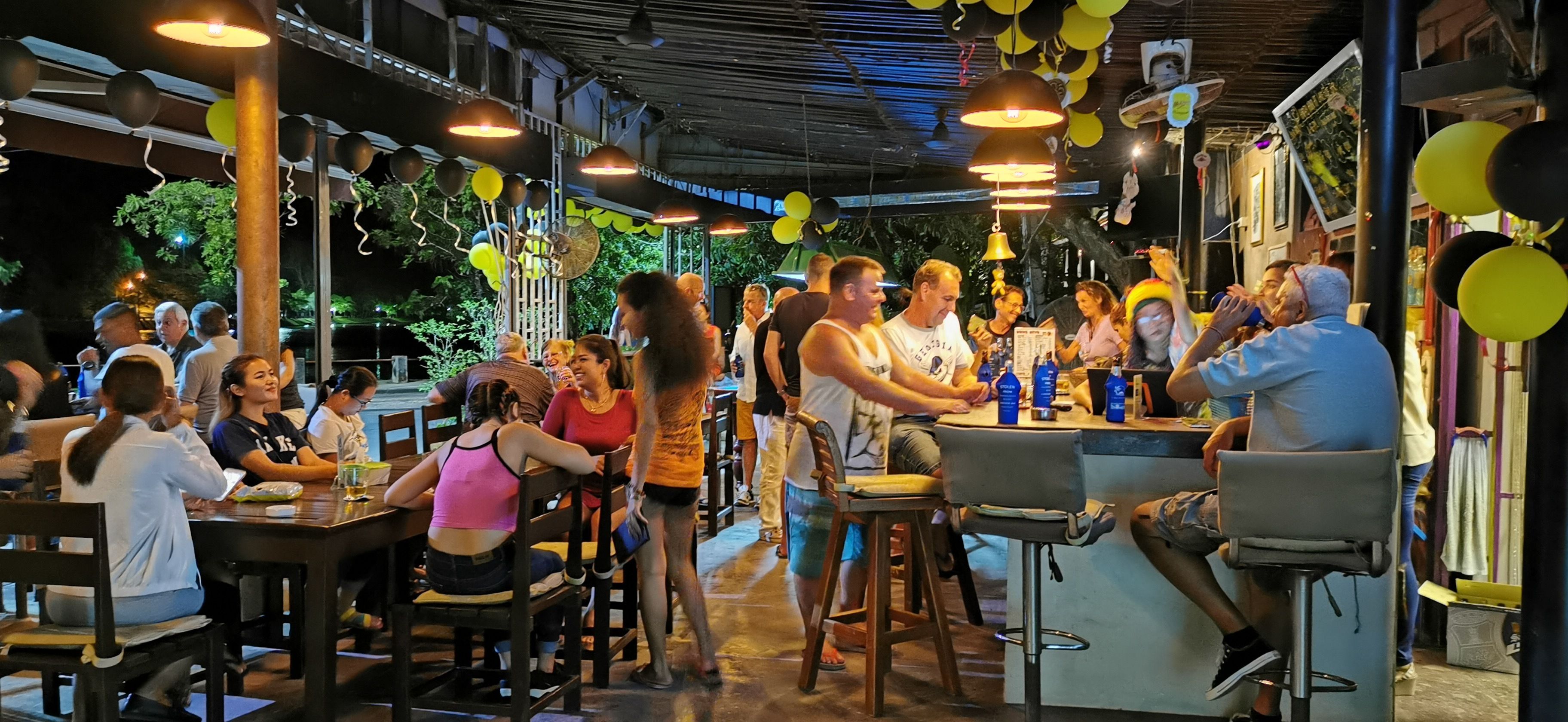 Un área de comedor al aire libre con mesas y sillas, rodeada de globos colgantes y luces colgantes.