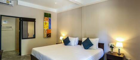 Una habitación de hotel con una cama grande, dos mesitas de noche con lámparas, un aire acondicionado instalado en la pared y una puerta que da a otra habitación.