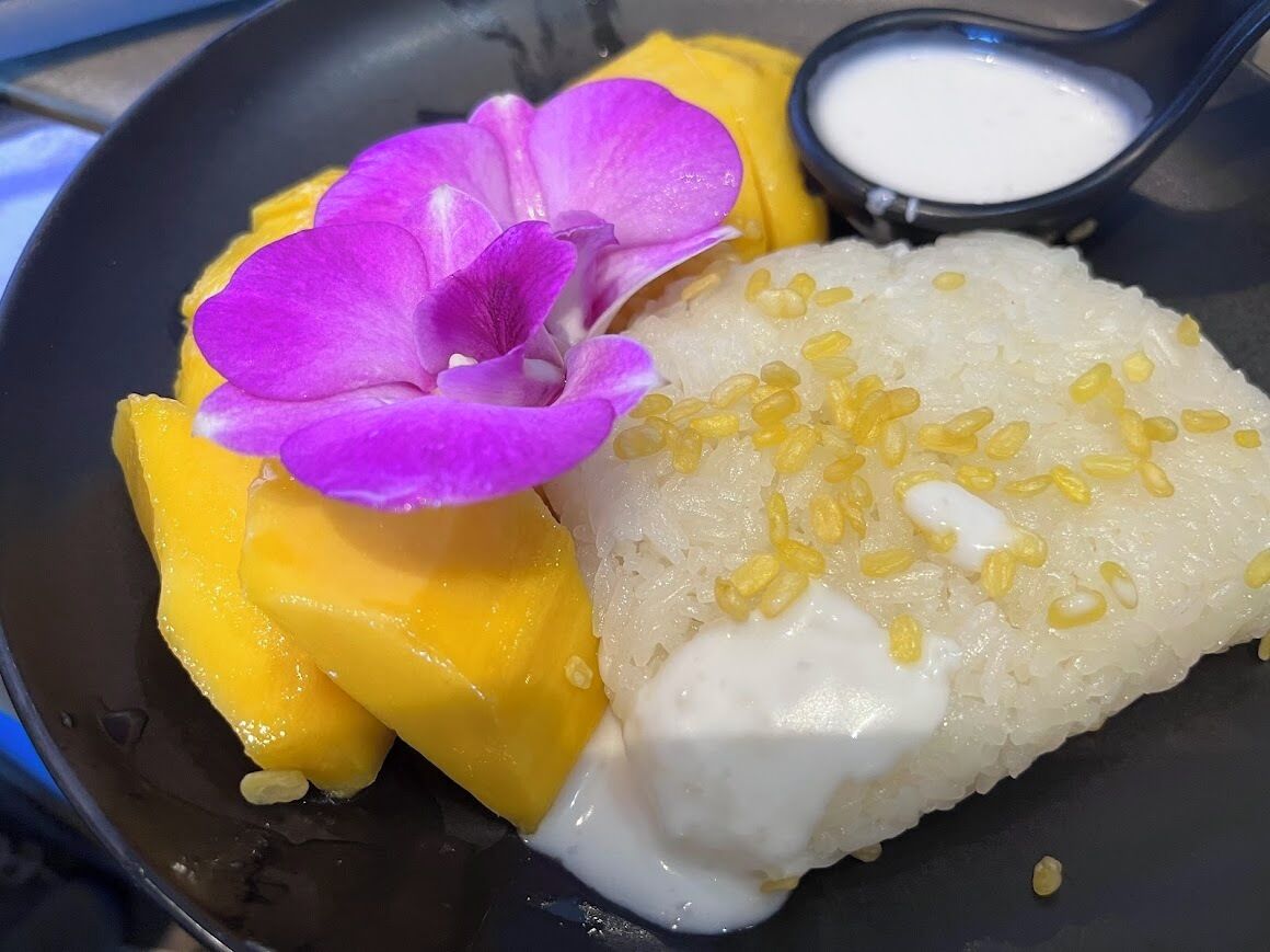 A plate with a dessert consisting of mango slices, a flower, and a creamy rice dish.