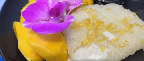 A plate with a dessert consisting of mango slices, a flower, and a creamy rice dish.
