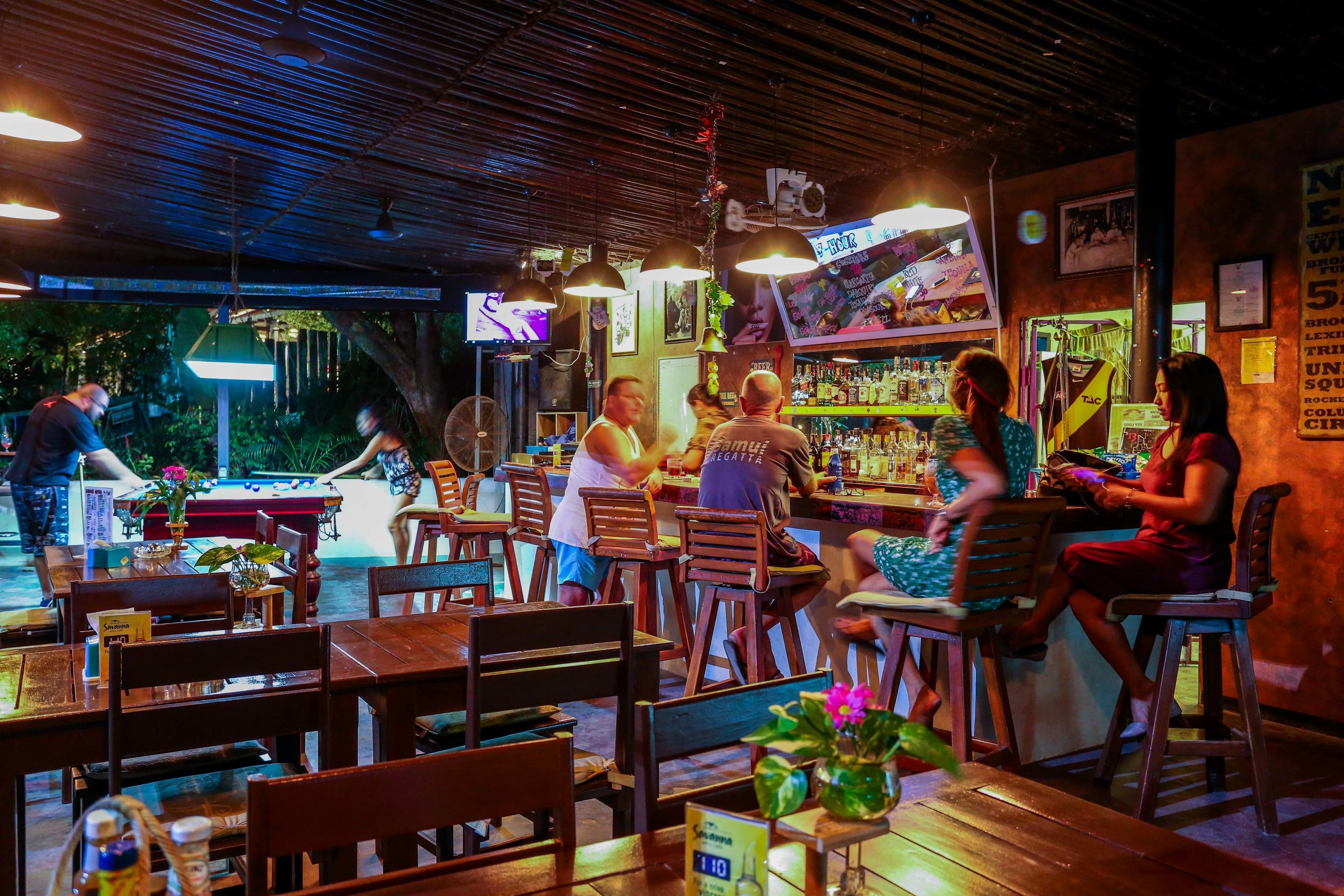 A restaurant with wooden tables and chairs, a bar area, and a television screen displaying content.