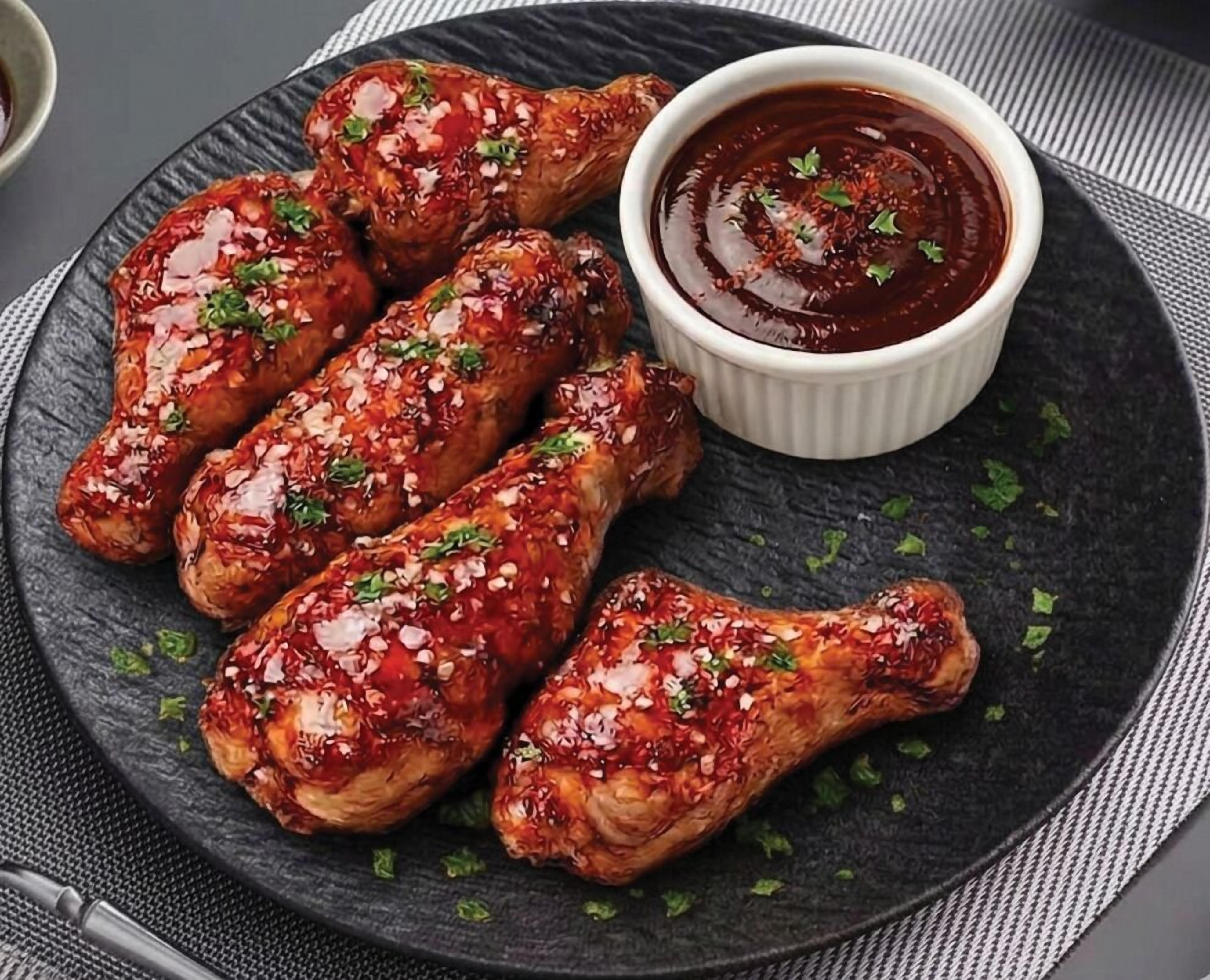 Een bord geglazuurde kippenvleugels met dipsaus.