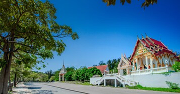A temple with a red roof and ornate decorations, surrounded by trees and a clear blue sky.
