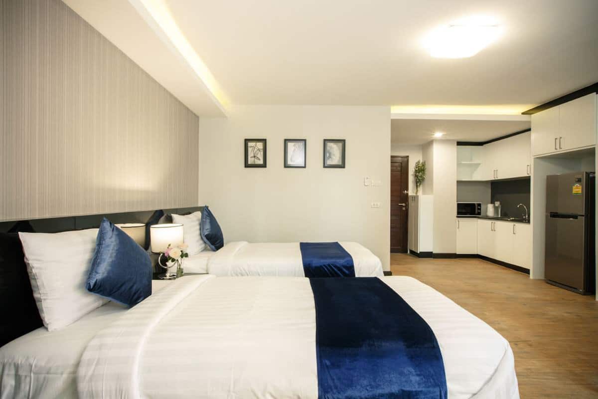 A hotel room with two beds, a kitchenette, and a bathroom visible in the background.