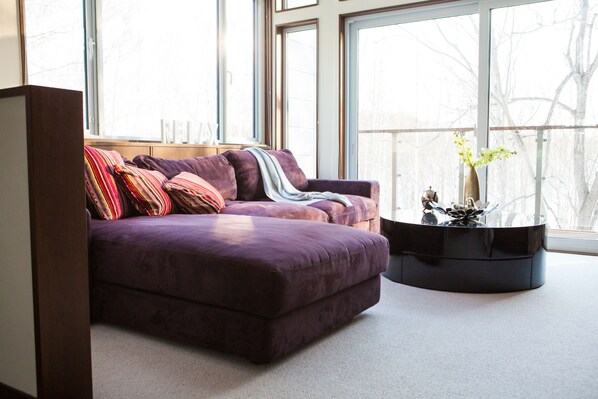 A modern living room with a purple sofa, a glass coffee table, and a vase with flowers.