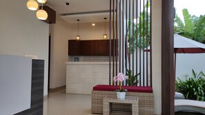 A modern reception area with a reception desk, a wicker bench with a red cushion, and a potted orchid. - Pondok Denayu Homestay (Kuta)