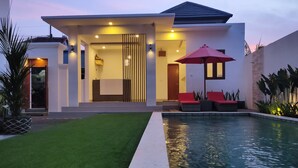 A modern house with a swimming pool, a covered patio with red cushions, and a well-maintained lawn. - Pondok Denayu Homestay (Kuta)