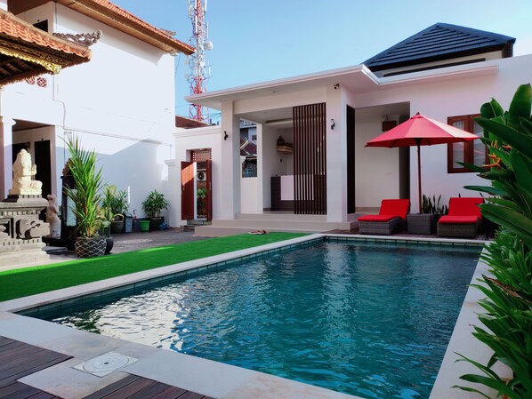 A modern house with a swimming pool, red outdoor furniture, and a statue.