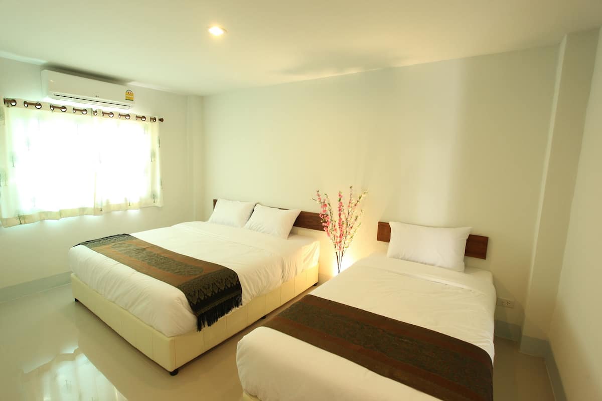 A hotel room with two beds, a window with curtains, an air conditioning unit, and a vase with flowers.