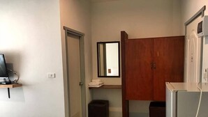 Une petite pièce propre, avec un lit, un bureau équipé d’un ordinateur, une armoire et un miroir.
