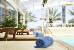 Un área junto a la piscina con sillones de madera, piscina y vista a palmeras.