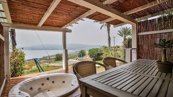 Um deck de madeira com uma banheira de hidromassagem, cadeiras de vime e vista para o mar.