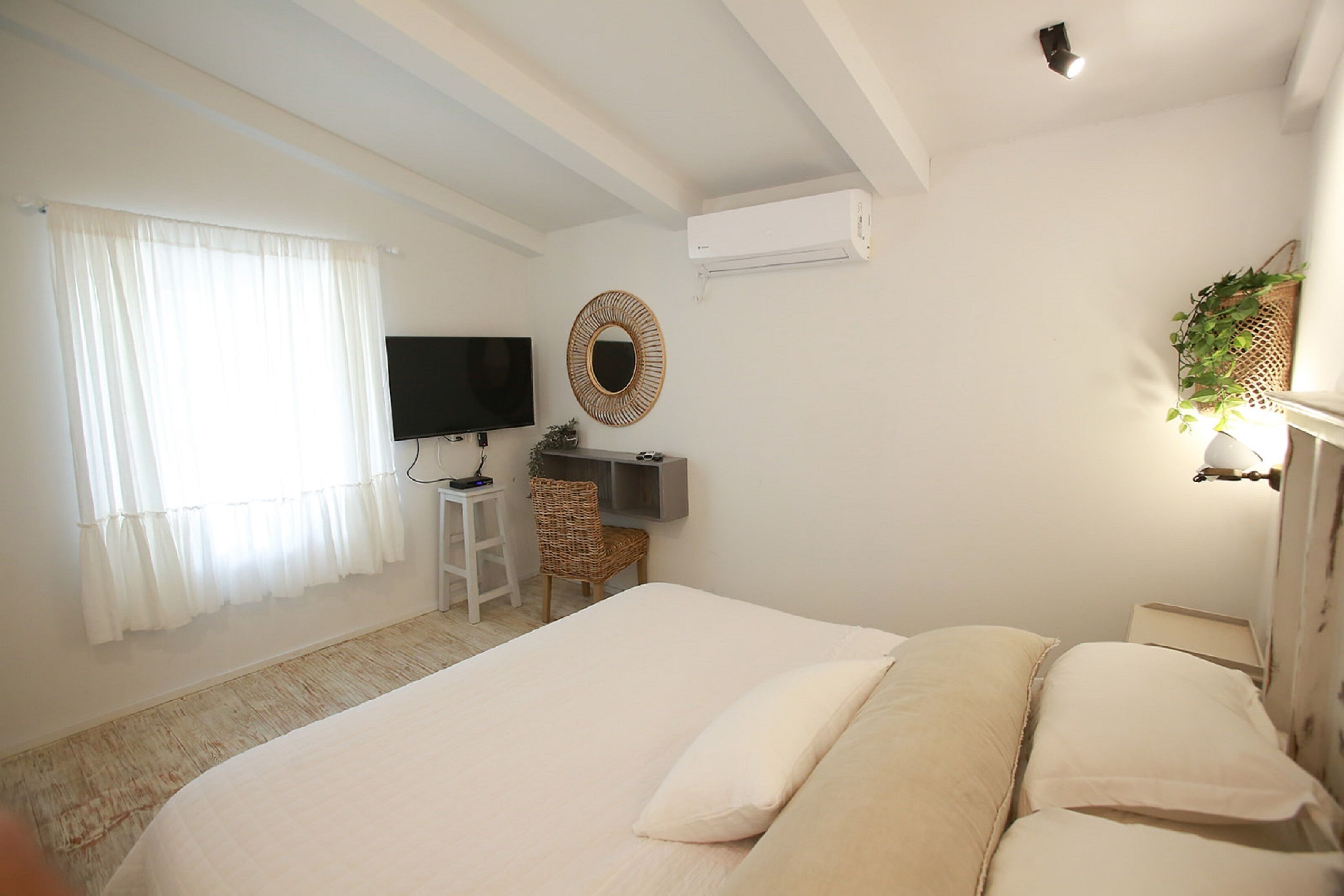 A bedroom with a bed, a desk, a television, and a wall-mounted air conditioner.