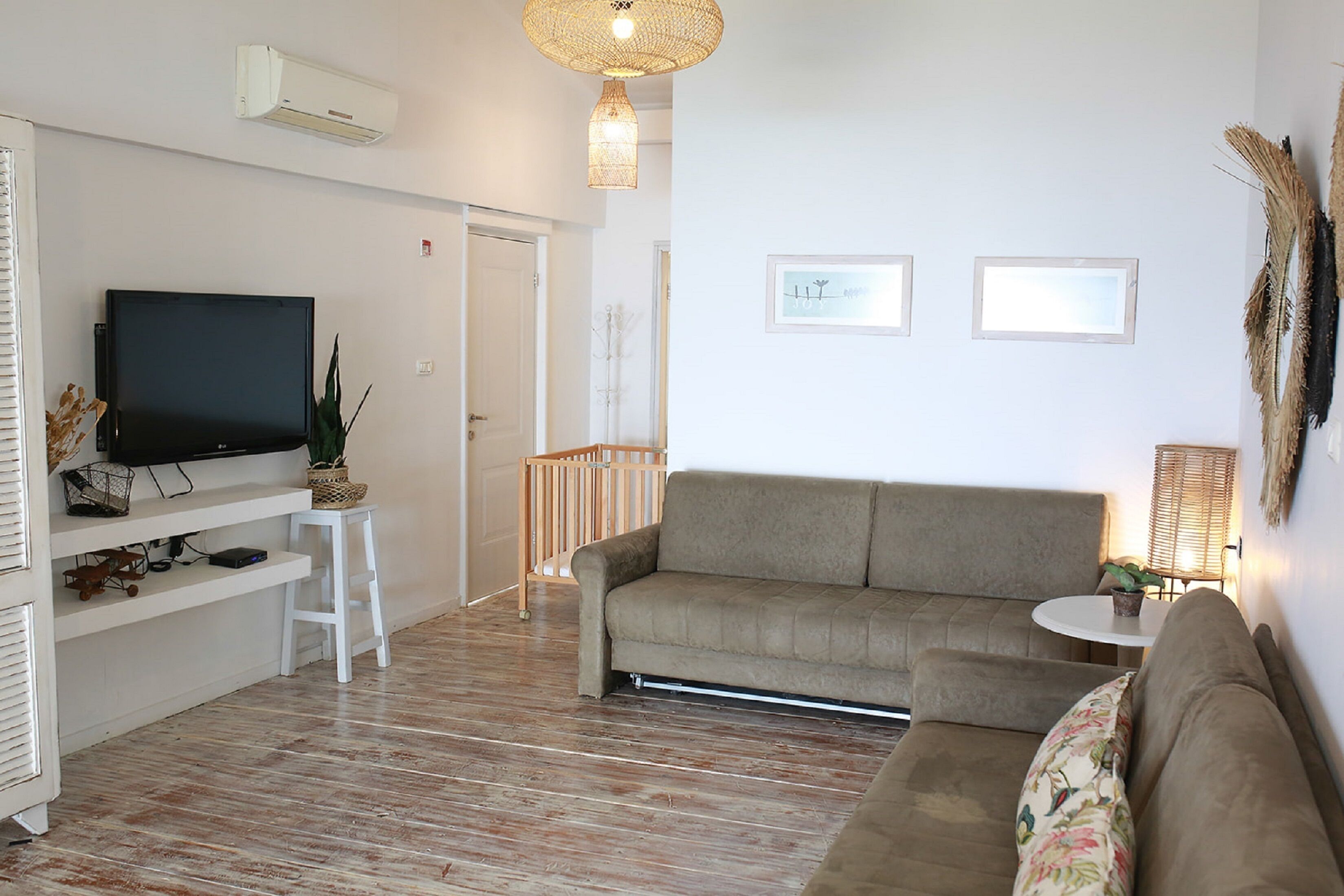 A living room with a sofa, a television, a small table, and a wicker lamp.