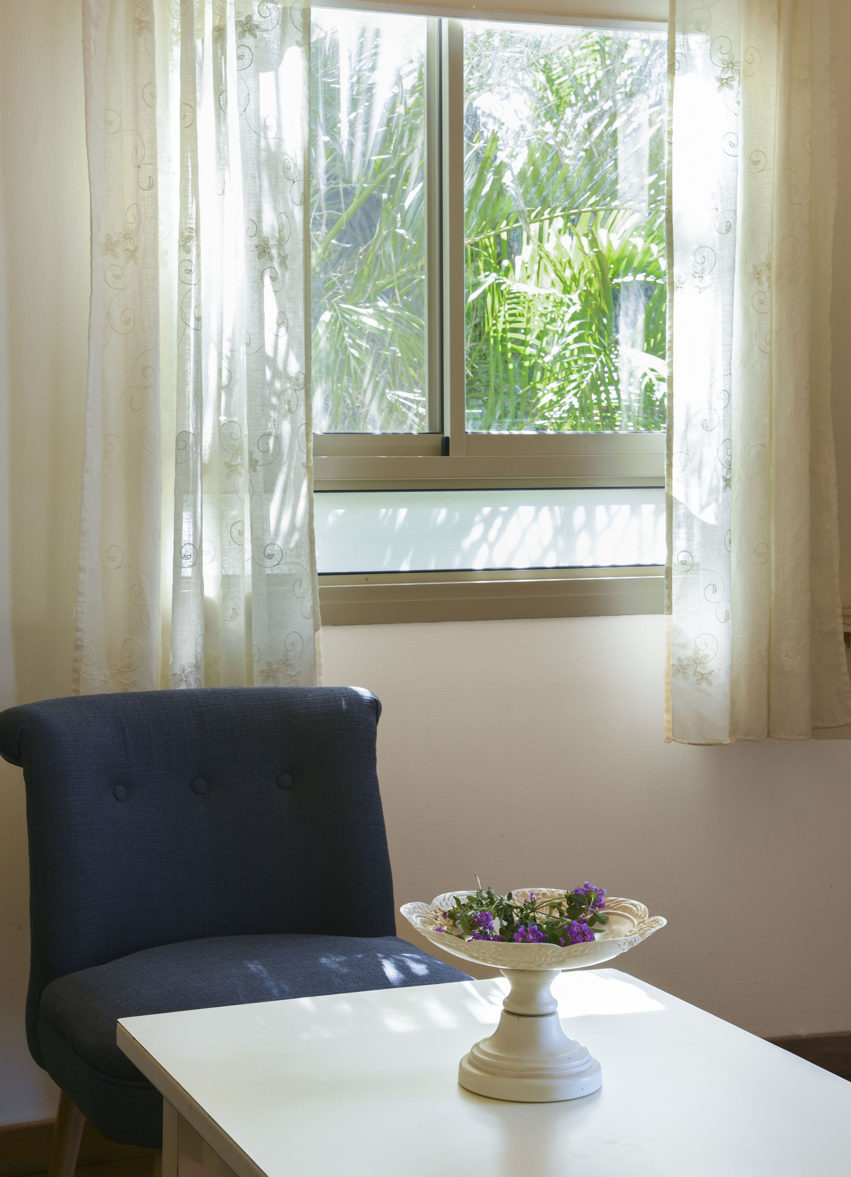 A room with a window, a chair, and a table with a decorative bowl.