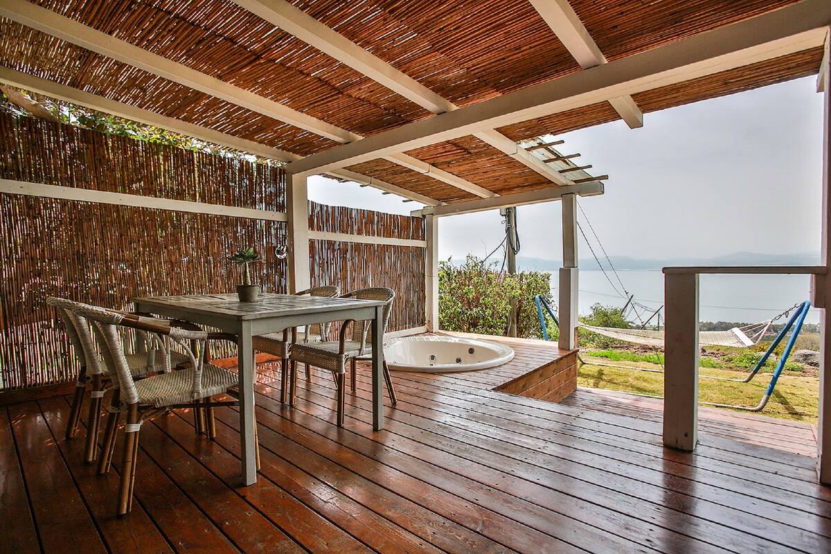 A wooden deck with a table and chairs, a hot tub, and a view of the sea.