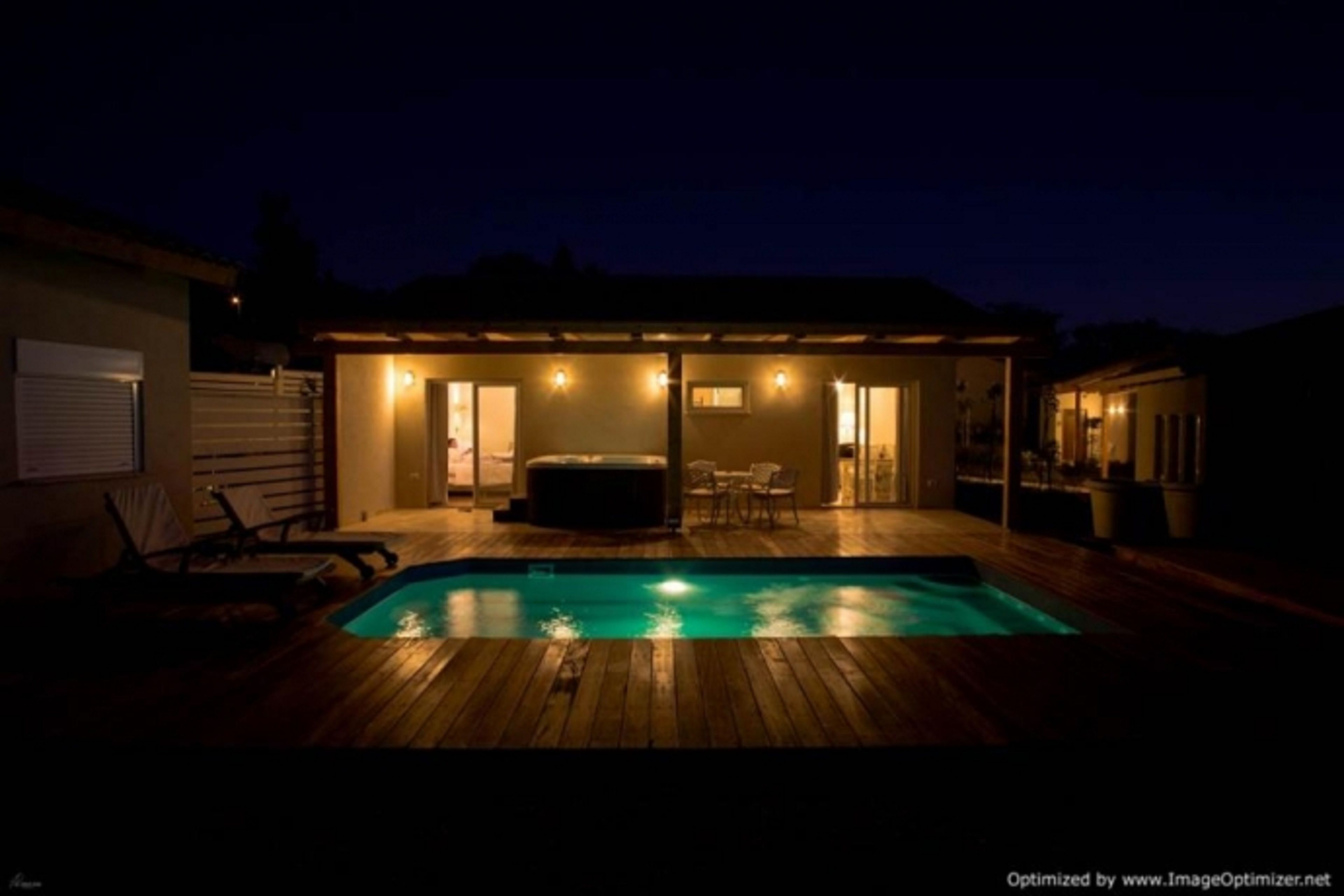 Piscina con muelle de madera, jacuzzi y zona de patio techada con sillas y mesas.