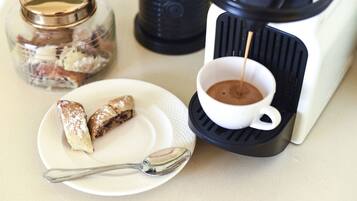 A coffee maker with a cup of coffee, a plate with pastries, and a jar of sugar.