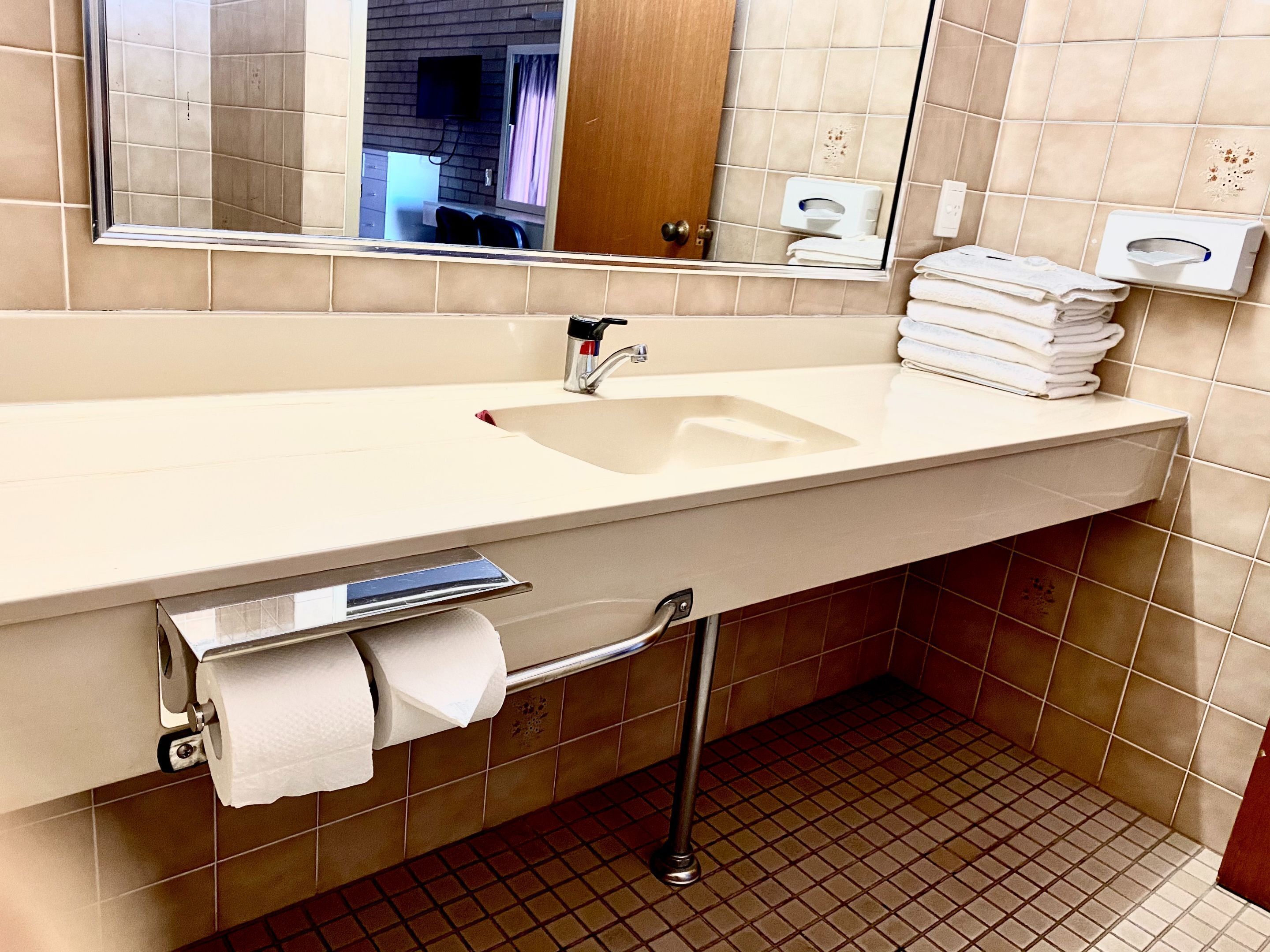 A bathroom with a sink, mirror, towel dispenser, and toilet paper holder.