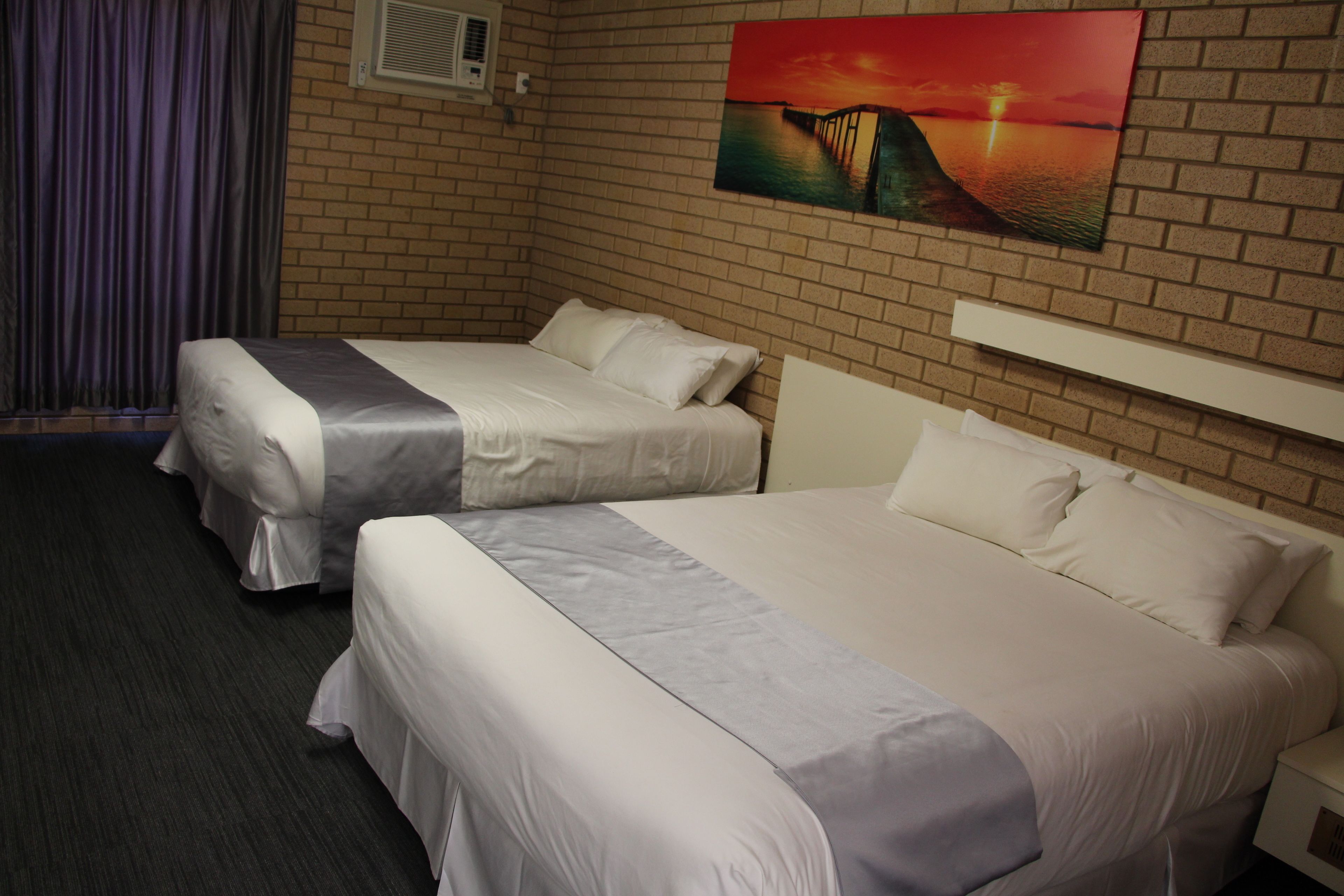 A hotel room with two beds, a brick wall, and a sunset painting.