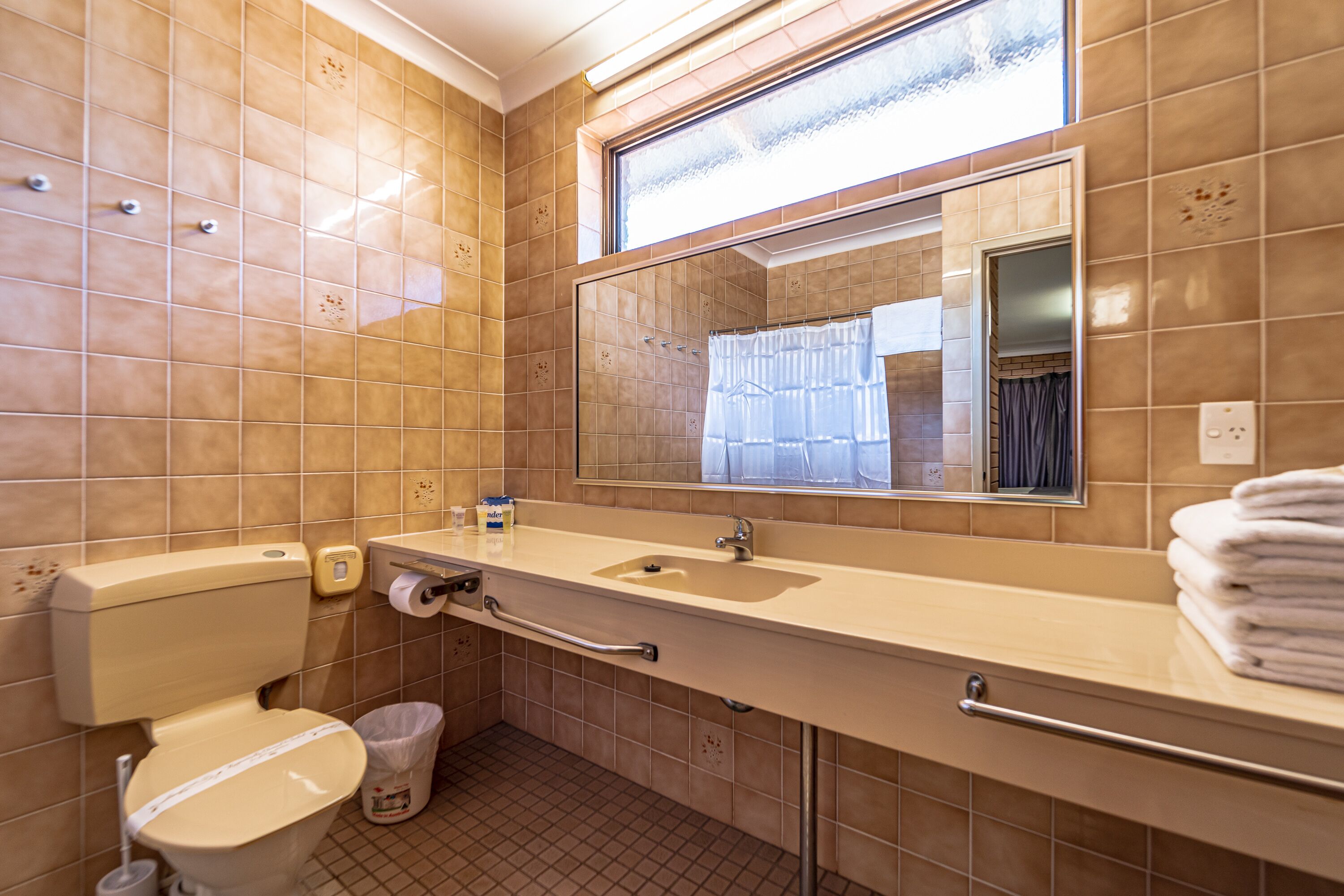 A bathroom with a toilet, sink, mirror, and window.