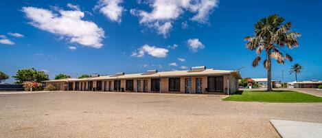 A motel with a parking lot, a palm tree, and a clear blue sky.