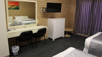 Quarto de hotel com cama, escrivaninha com cadeira, penteadeira, televisão presa na parede e um quadro com um pôr do sol sobre uma ponte.