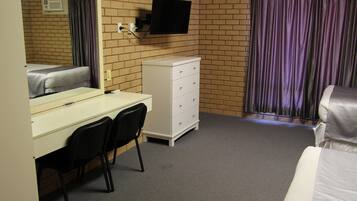 A hotel room with a bed, a desk with a chair, a dresser, a television mounted on the wall, and a window with curtains.