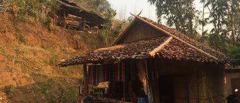 A rustic wooden structure with a thatched roof, a small shop with colorful items outside, and a dirt path leading to it.
