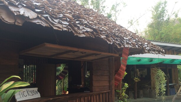 A wooden building with a thatched roof, a wooden porch, and a sign indicating a price of $100. - Suan Pra - Inn (Pai)