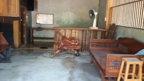 A room with a wooden bench, a small stool, a fan, and a window with bars. - Suan Pra - Inn (Pai)
