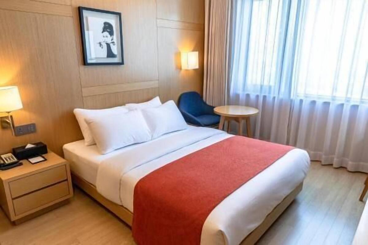 A hotel room with a bed, bedside table, lamp, chair, and a small table.