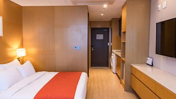 Habitación de hotel con una cama, una manta roja, un televisor, una lavadora y un armario de madera.