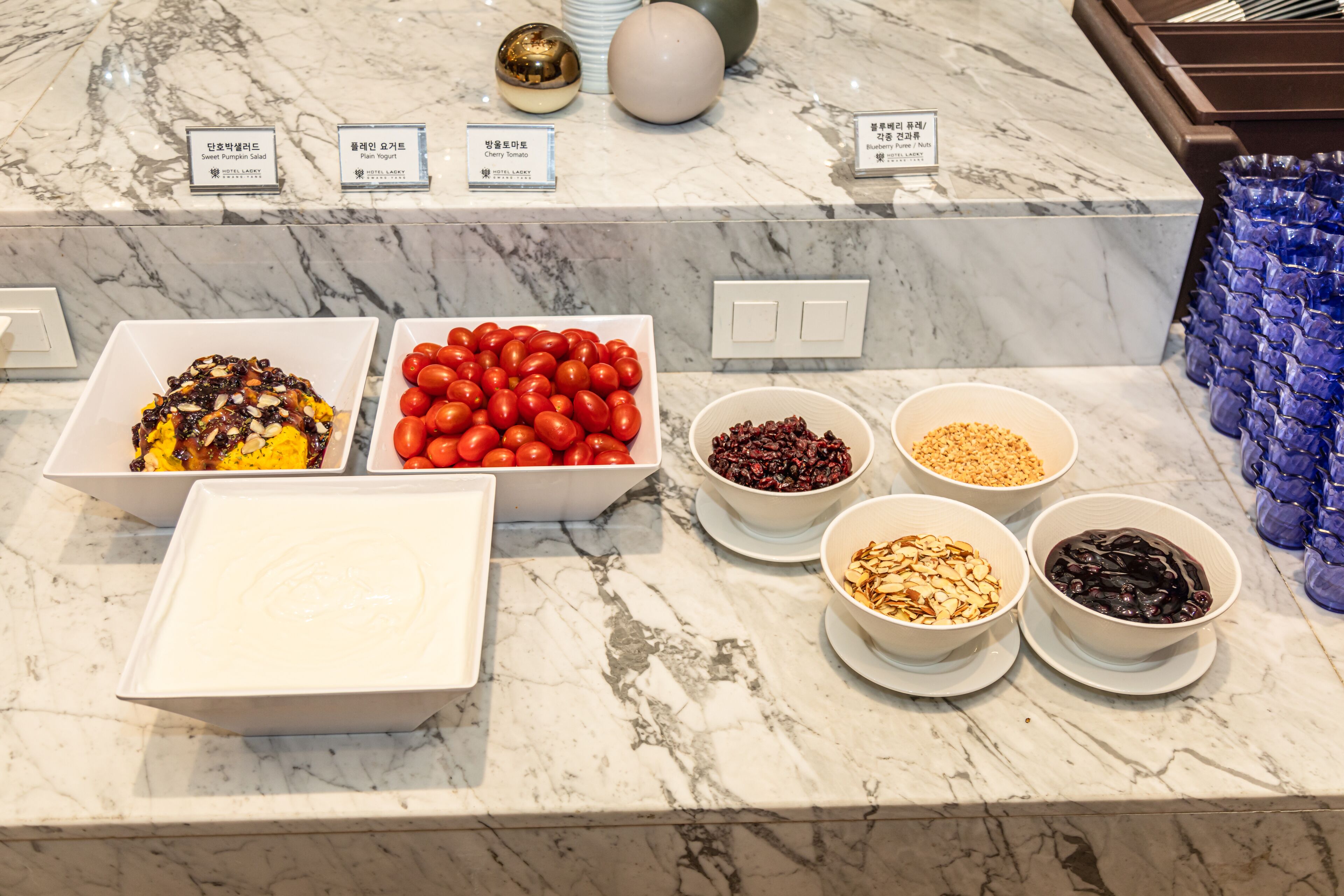 A buffet with various food items including sweet pumpkin salad, plum yogurt, cherry tomatoes, and bowls of mixed nuts and berries.