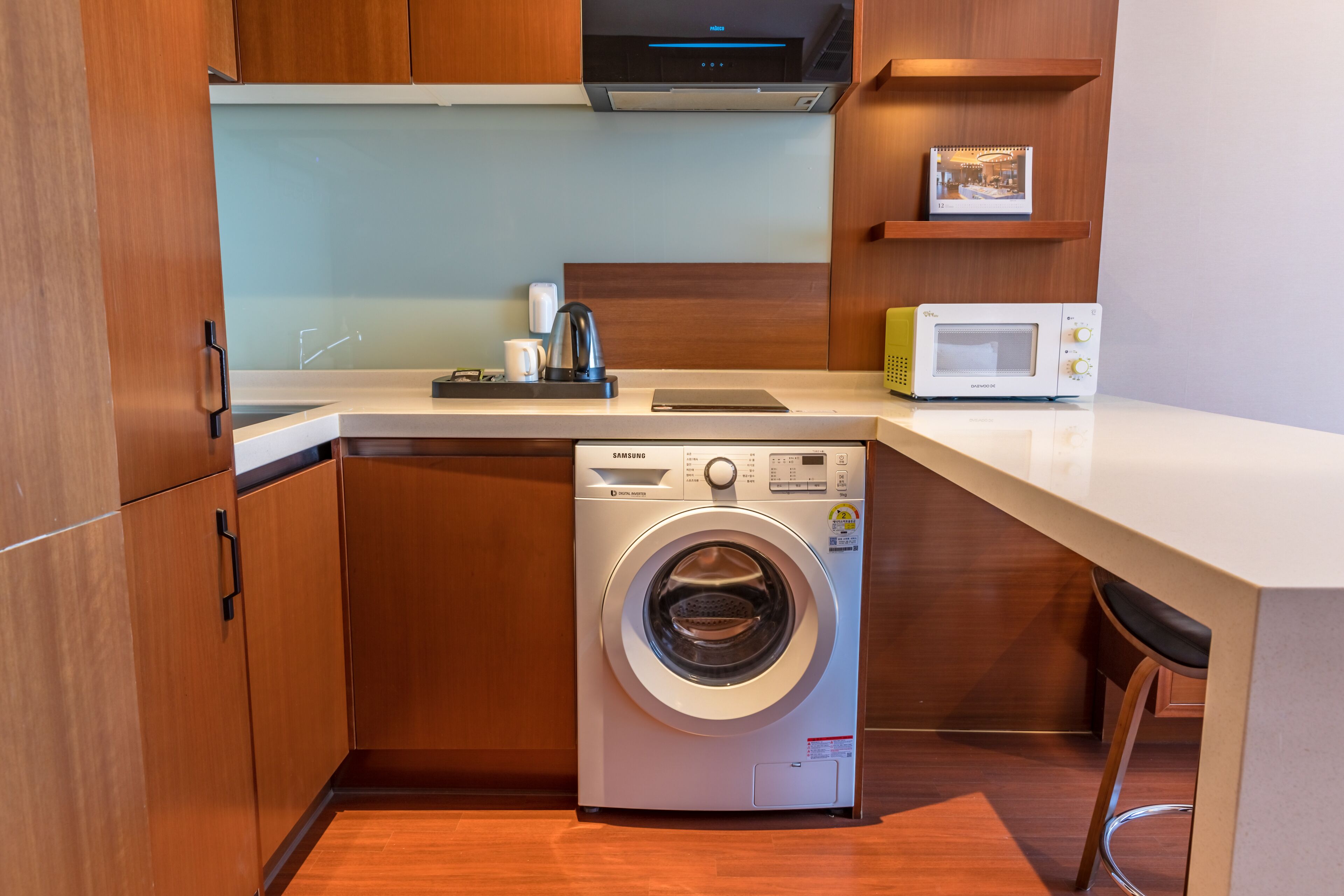 Una cocina compacta con lavadora y secadora integradas, armarios de madera, un microondas y una pequeña encimera.