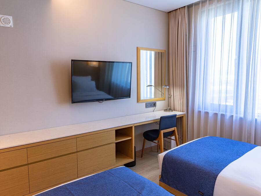A hotel room with a bed, a desk, a chair, a television, and a window with curtains.