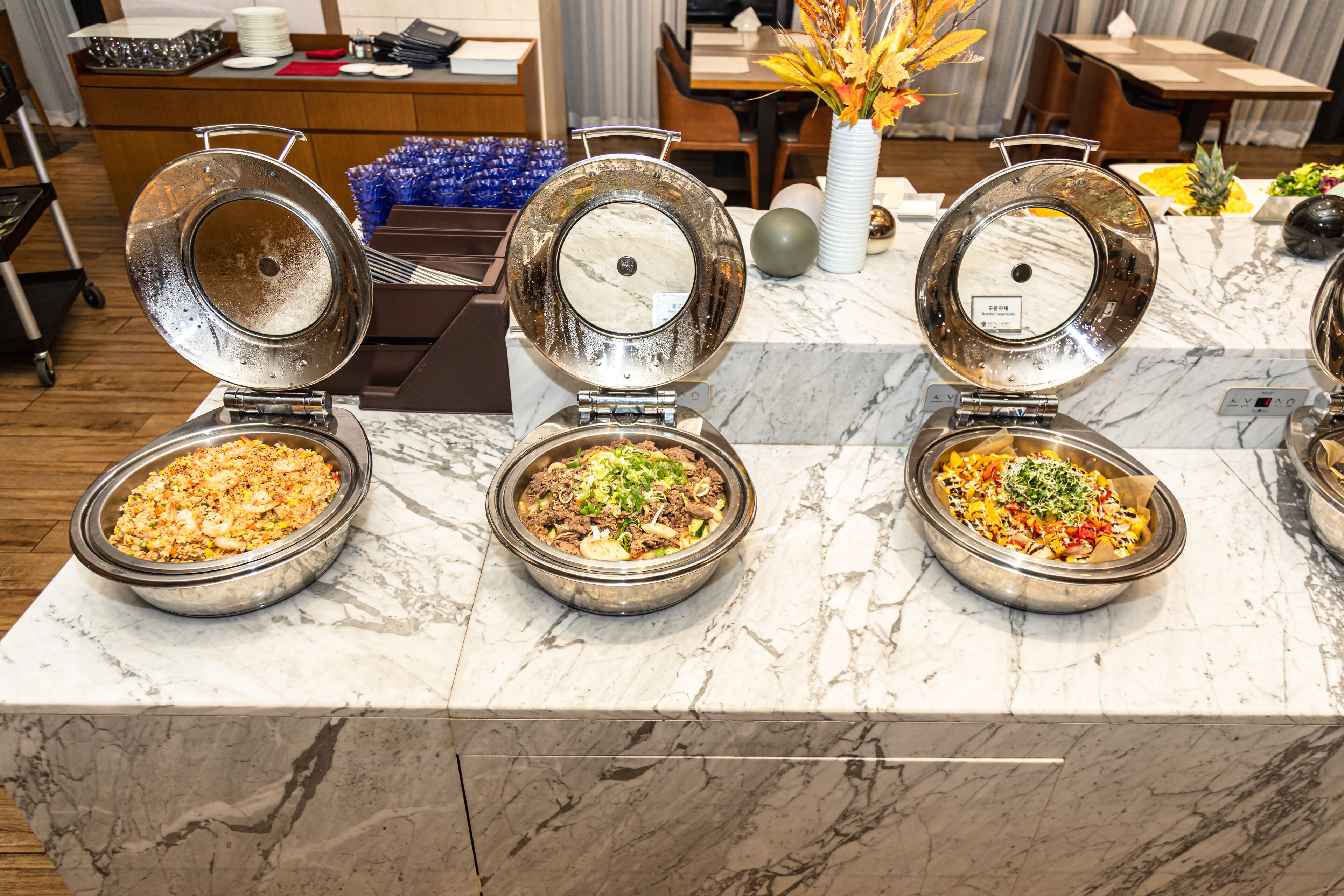 A buffet with three open bowls of food on a marble countertop.
