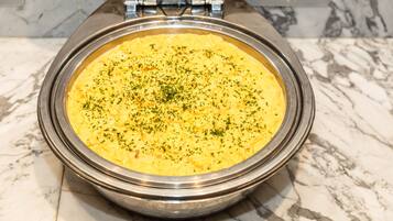 A large metal serving dish with a creamy yellow dish, possibly a casserole, garnished with herbs, placed on a marble countertop.