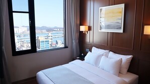 A hotel room with a large bed, a view of a cityscape through a window, and a framed picture on the wall. - Hotel Lacky Gwangyang (Gwangyang)