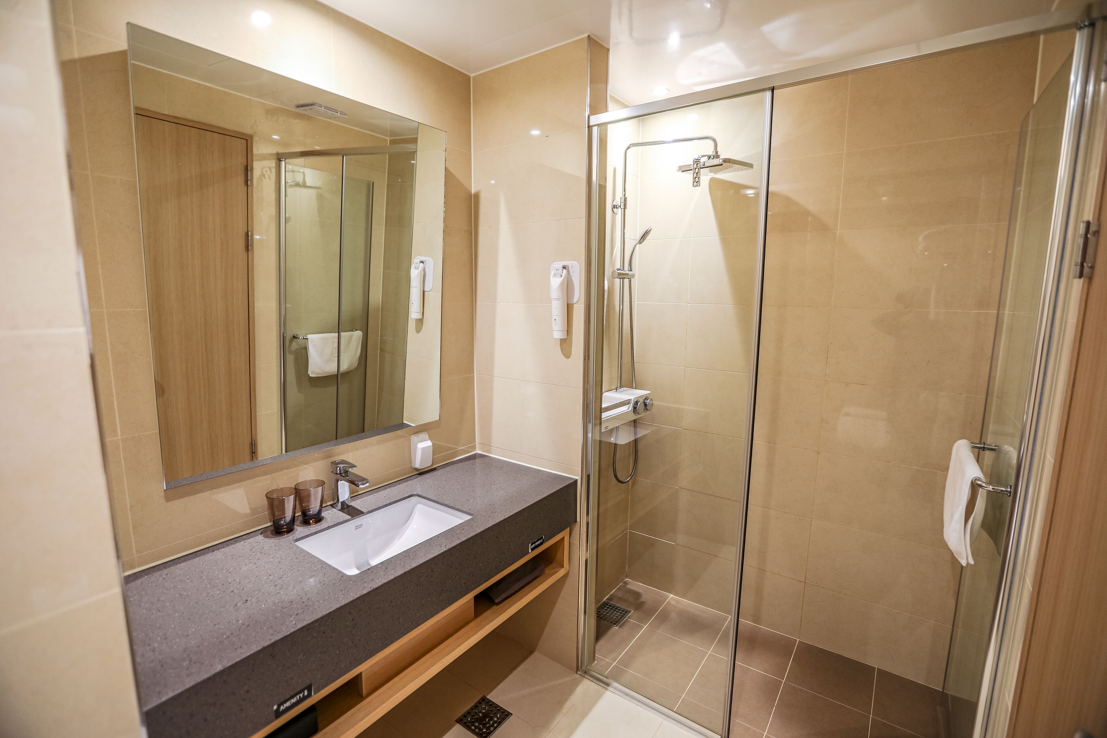 Un baño moderno con ducha acristalada, lavamanos con espejo y un perchero para toallas.
