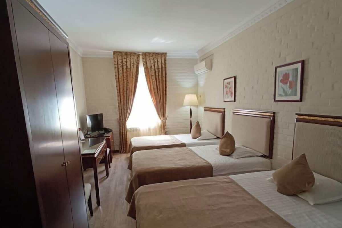 A hotel room with two beds, a desk with a television, a wardrobe, and a window with curtains.