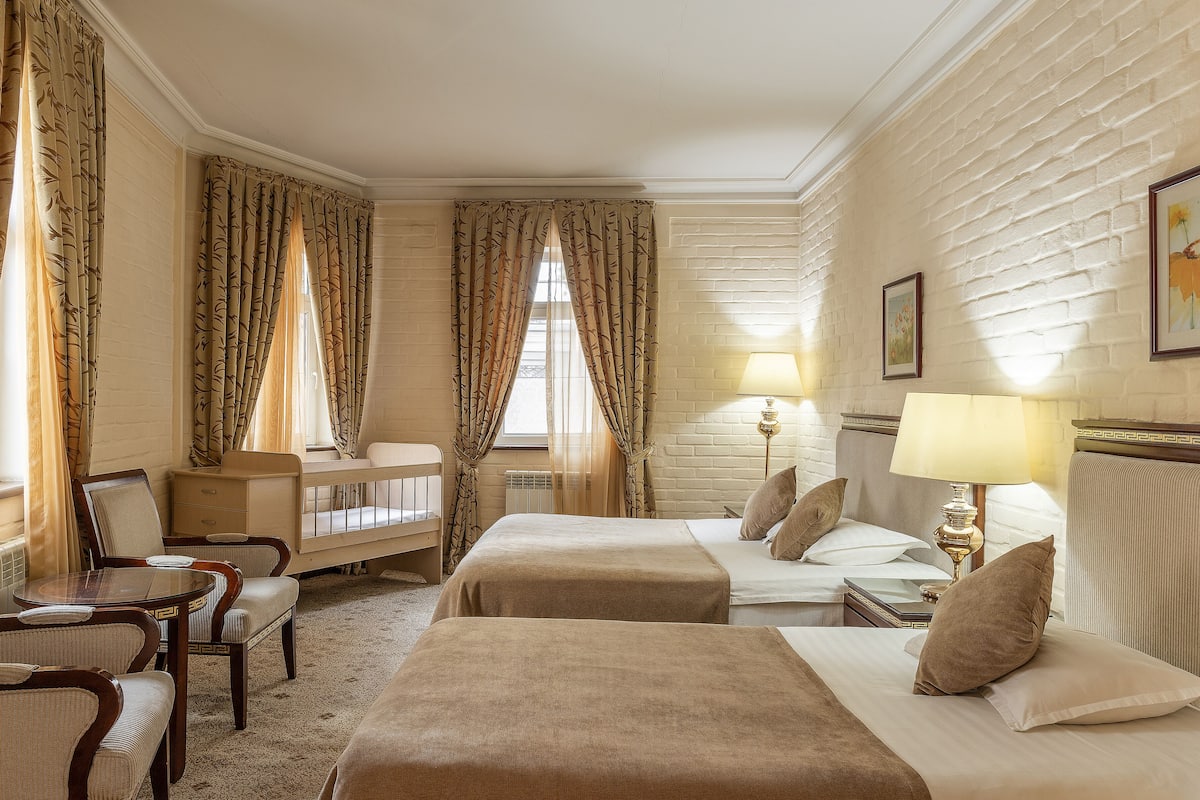 A hotel room with two beds, a desk, chairs, and a window with curtains.